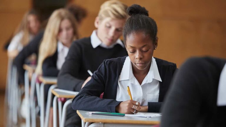 Teenage Students In Uniform Sitting Examination In School Hall