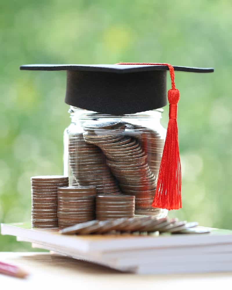 Graduation hat on coins money in the glass bottle on natural green background, Saving money for education