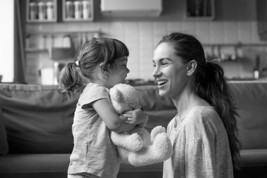 Woman smiling at girl holding a teddy bear