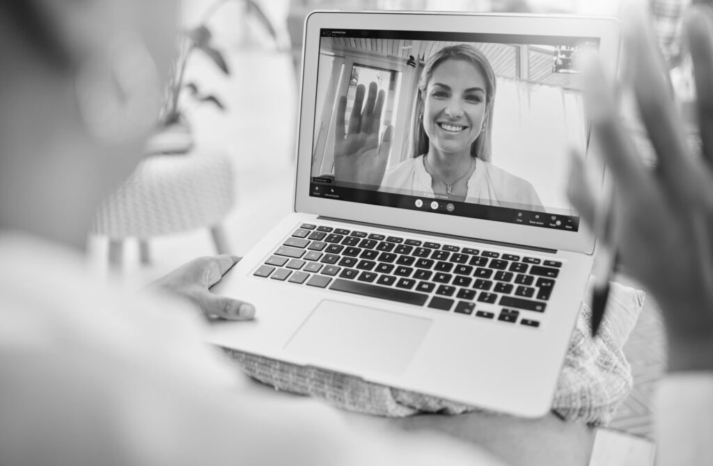 Woman on laptop screen smiling and waving