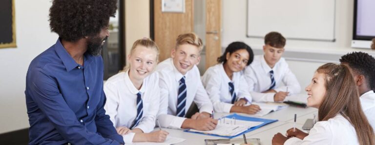 Black teacher sitting down talking to classroom