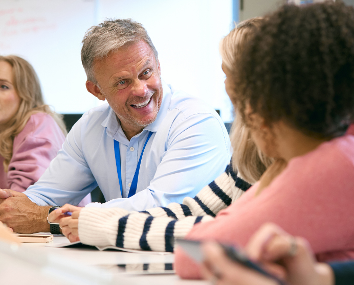 Senior teacher talking to his colleagues in the staff room before a meeting starts.