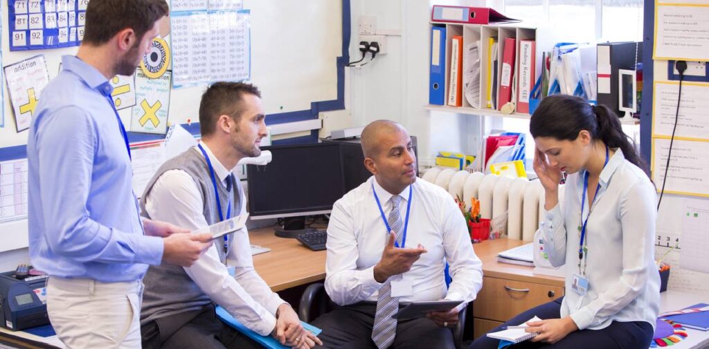 Stressed teachers in staffroom comforting a colleague as she is struggling with mental health.