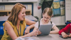 SEND Teaching Assistant supporting child with down syndrome with a tablet in the chlassroom