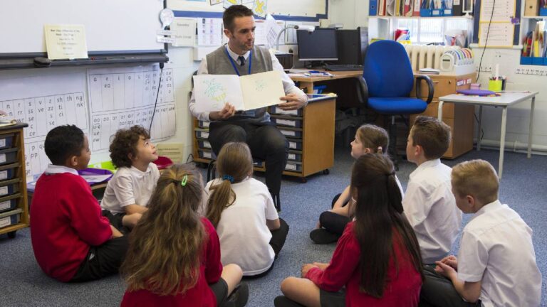 White male cover supervisor in a UK primary school, having story time with his class