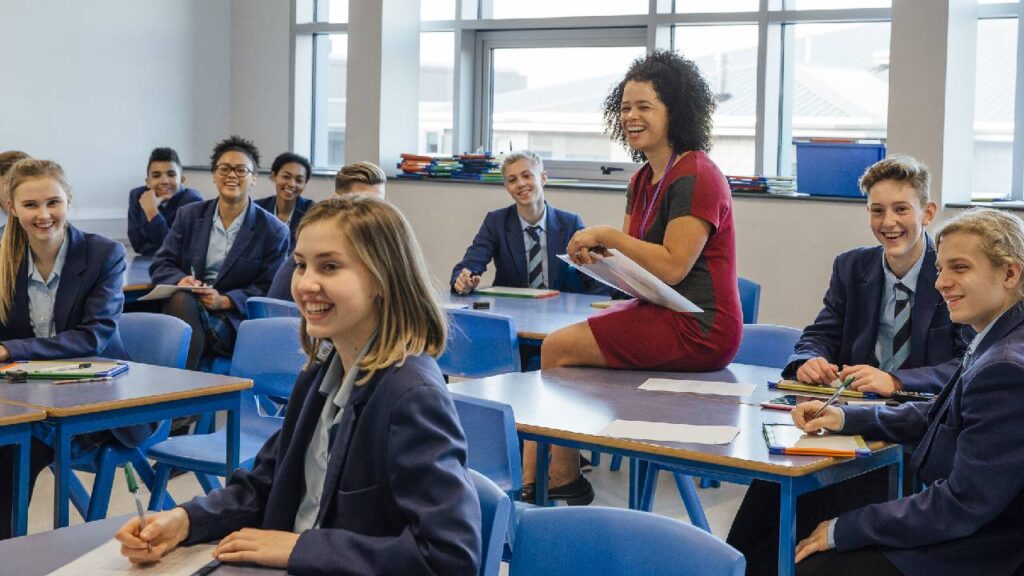 Mixed race female cover supervisor in a UK secondary school laughing with her classroom