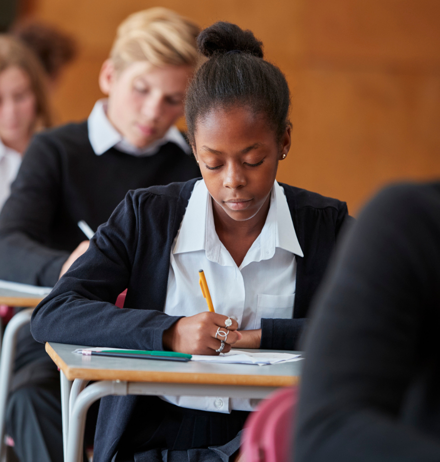 Teenage Students In Uniform Sitting Examination In School Hall