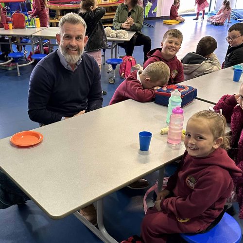 Paul Broderick sitting with school children eating breakfast